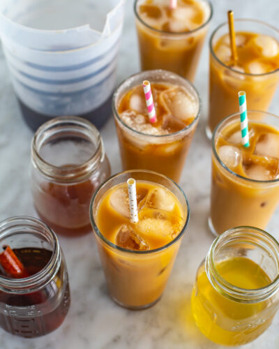 6 glasses of cold brew coffee next to a pitcher and different homemade cold brew syrups.