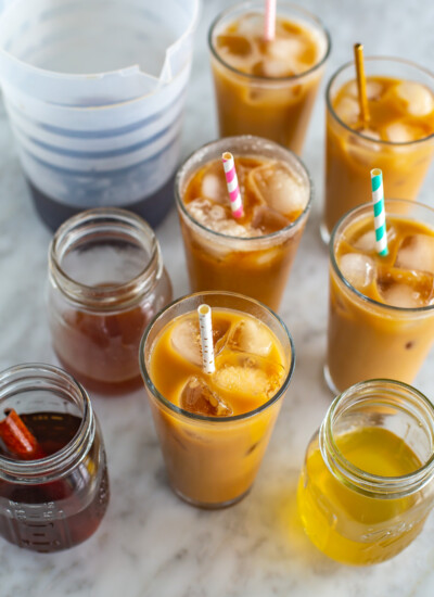 6 glasses of cold brew coffee next to a pitcher and different homemade cold brew syrups.
