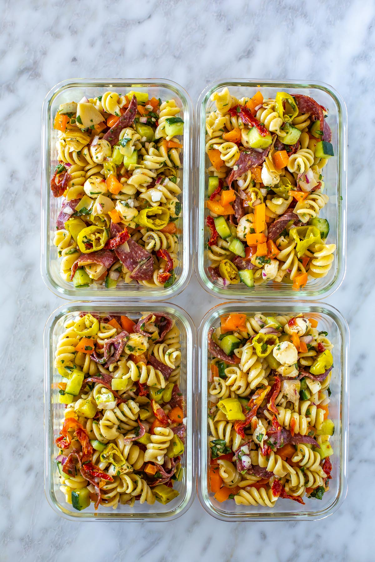 Four meal prep containers, each filled with Italian pasta salad.