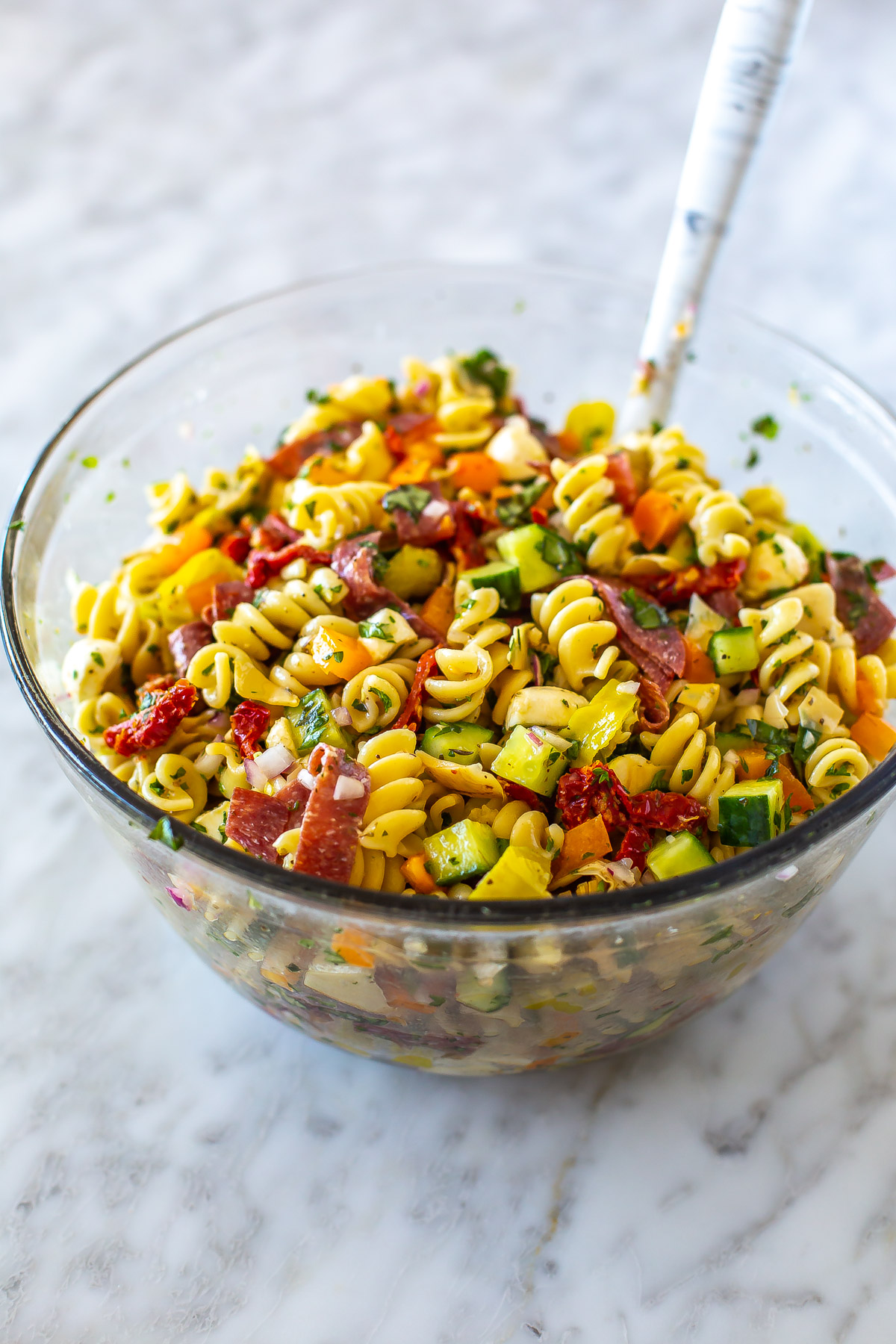 A big bowl filled with Italian pasta salad with a spoon in it.