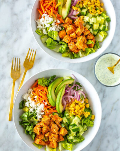 Two bowls of buffalo chicken salad next to each other with ranch dressing on the side.