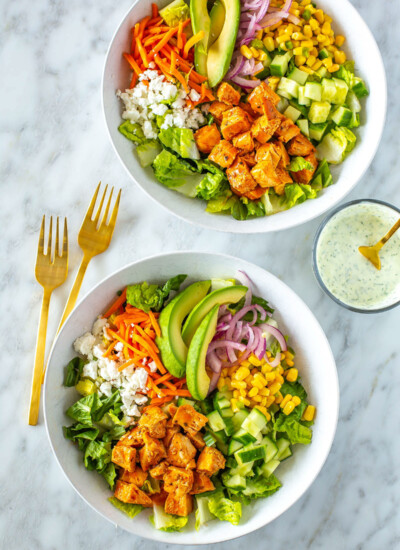 Two bowls of buffalo chicken salad next to each other with ranch dressing on the side.