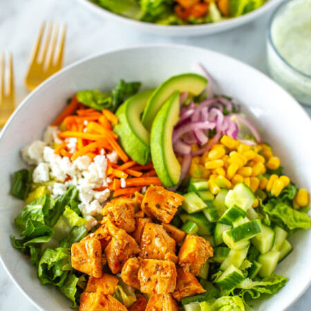 A close-up of a bowl of buffalo chicken salad with a bowl of ranch dressing on the side.