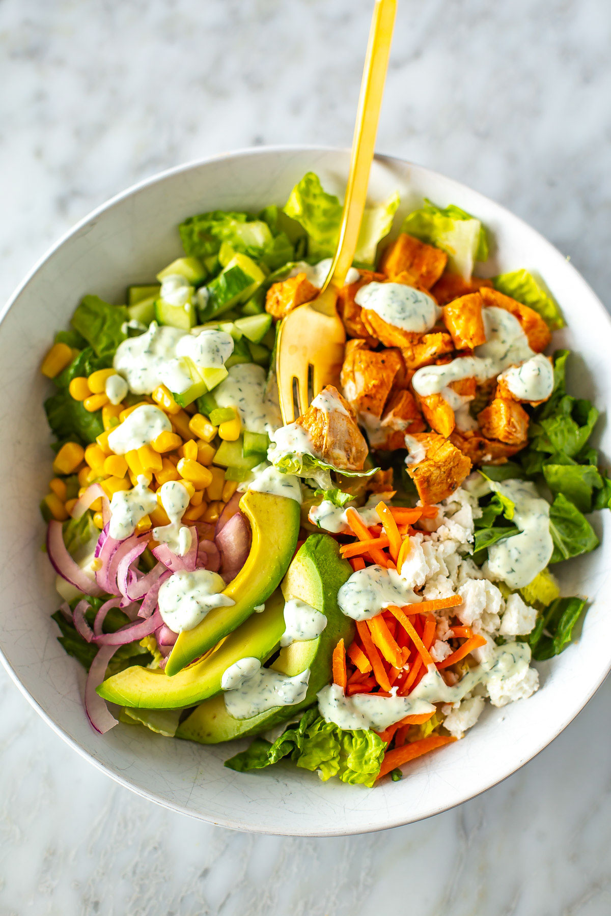 A close-up of a bowl of buffalo chicken salad with ranch dressing drizzled over top.