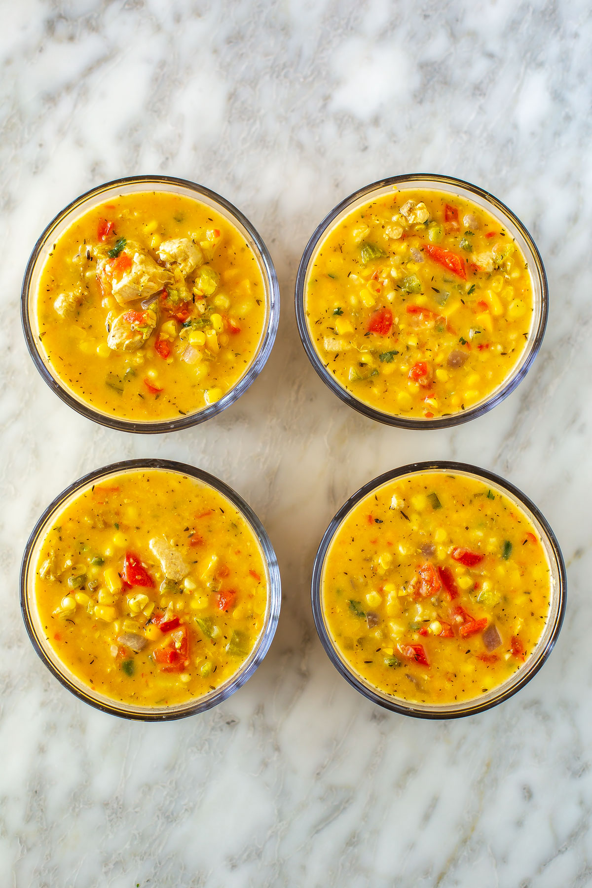 Four round glass containers, each filled with chicken corn chowder.