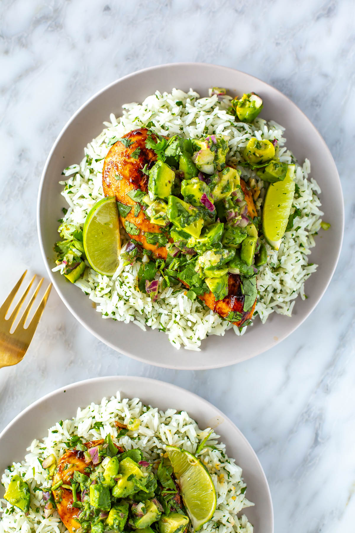 A close-up of cilantro lime chicken and rice on a plate topped with avocado salsa.