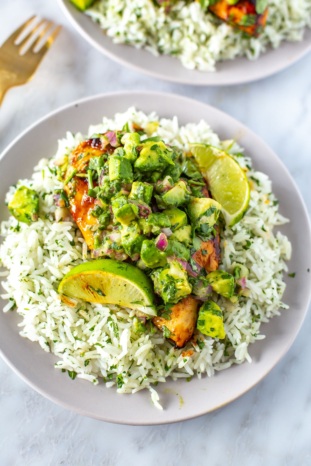 A close-up of cilantro lime chicken and rice on a plate topped with avocado salsa.