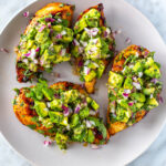 Four cilantro lime chicken cutlets on a plate, each topped with avocado salsa.