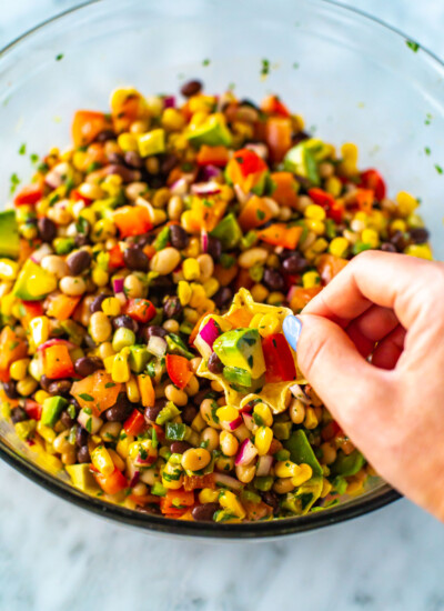 A hand with a tortilla chip scooping up cowboy caviar from a bowl.