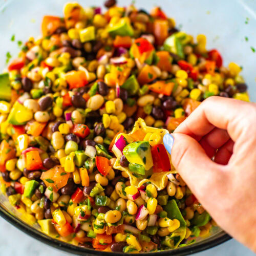 A hand with a tortilla chip scooping up cowboy caviar from a bowl.