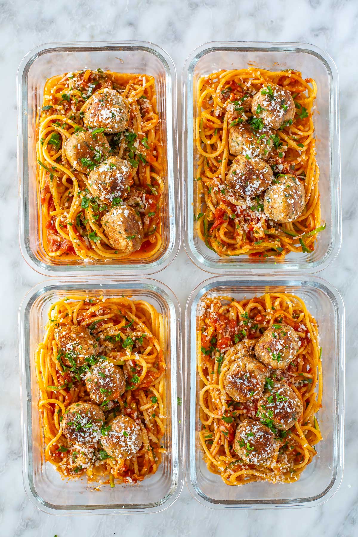 Four meal prep containers, each with a serving of turkey meatballs with pasta and zucchini noodles.