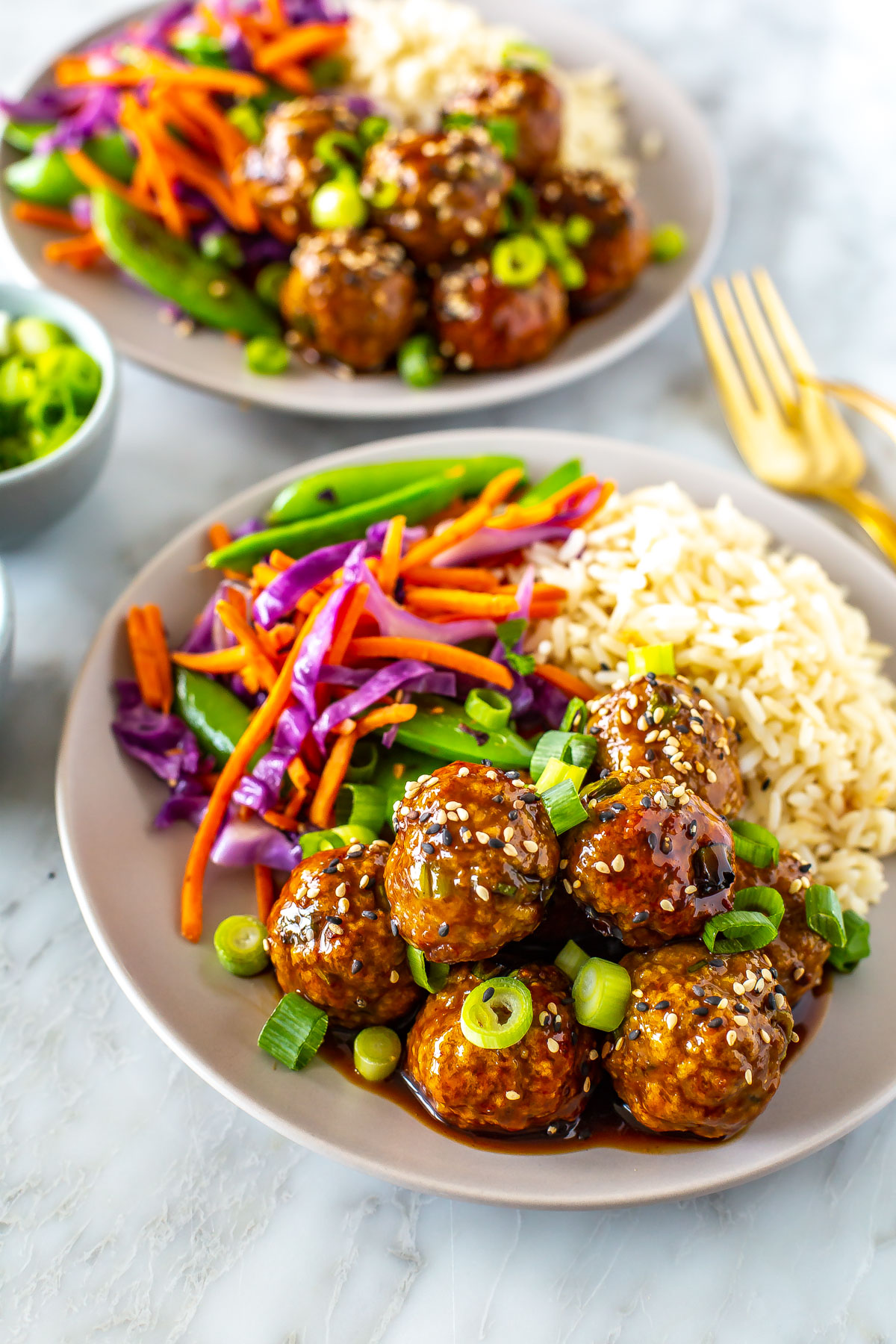 A close-up of a bowl with a bed of rice, side of stir fried veggies and sticky teriyaki chicken meatballs.