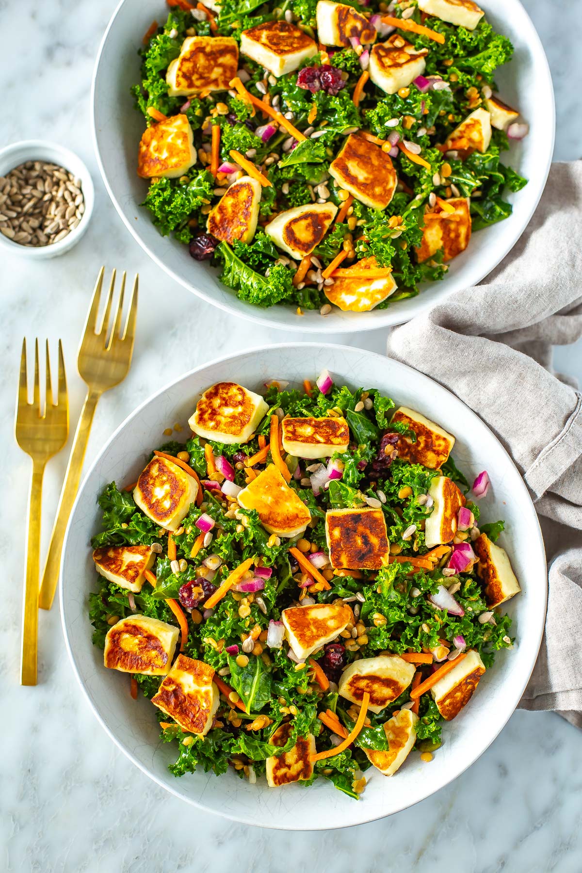 Two bowls filled with kale salad topped with cooked halloumi cheese.