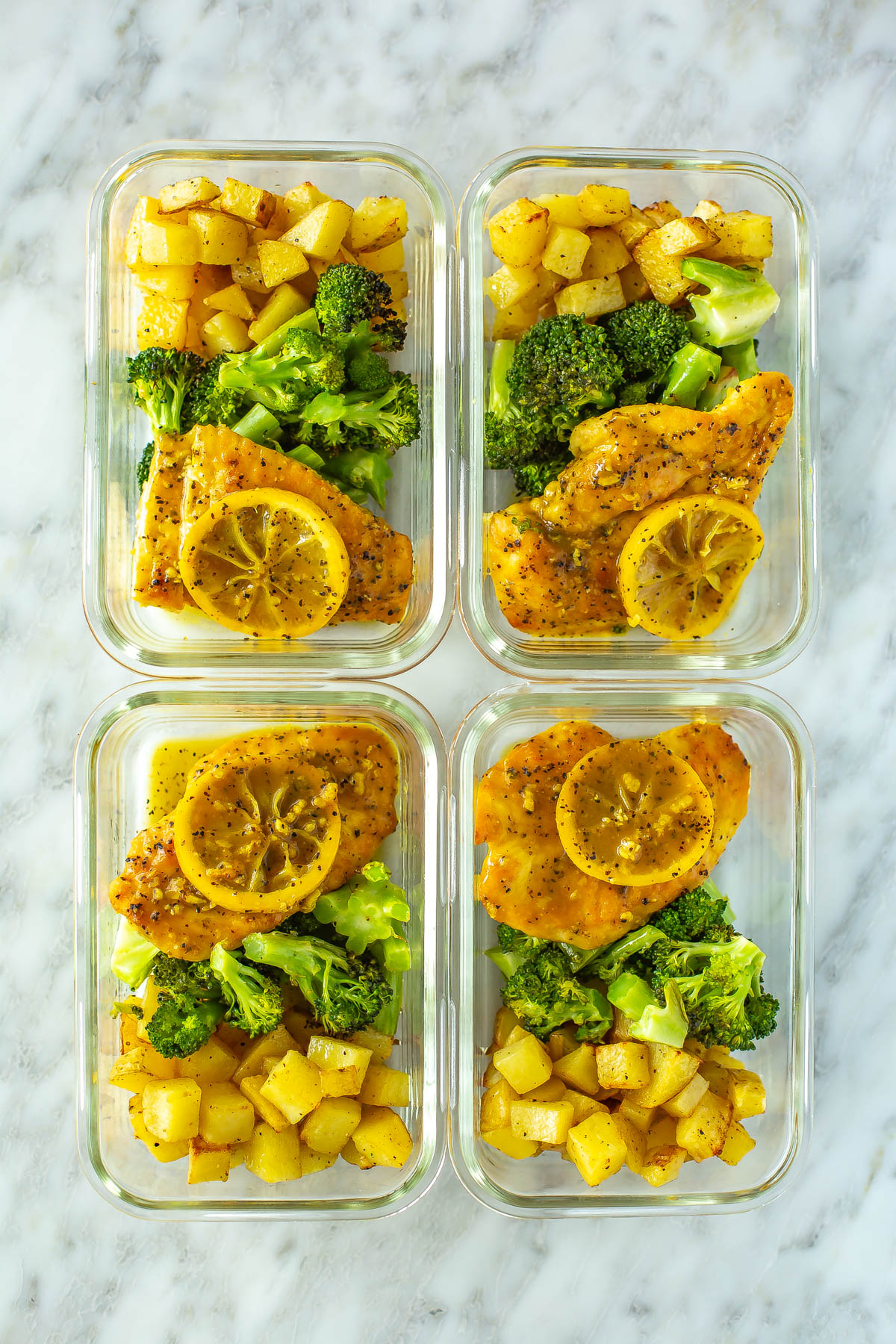 Four meal prep containers, each with lemon pepper chicken, roasted potatoes and roasted broccoli.