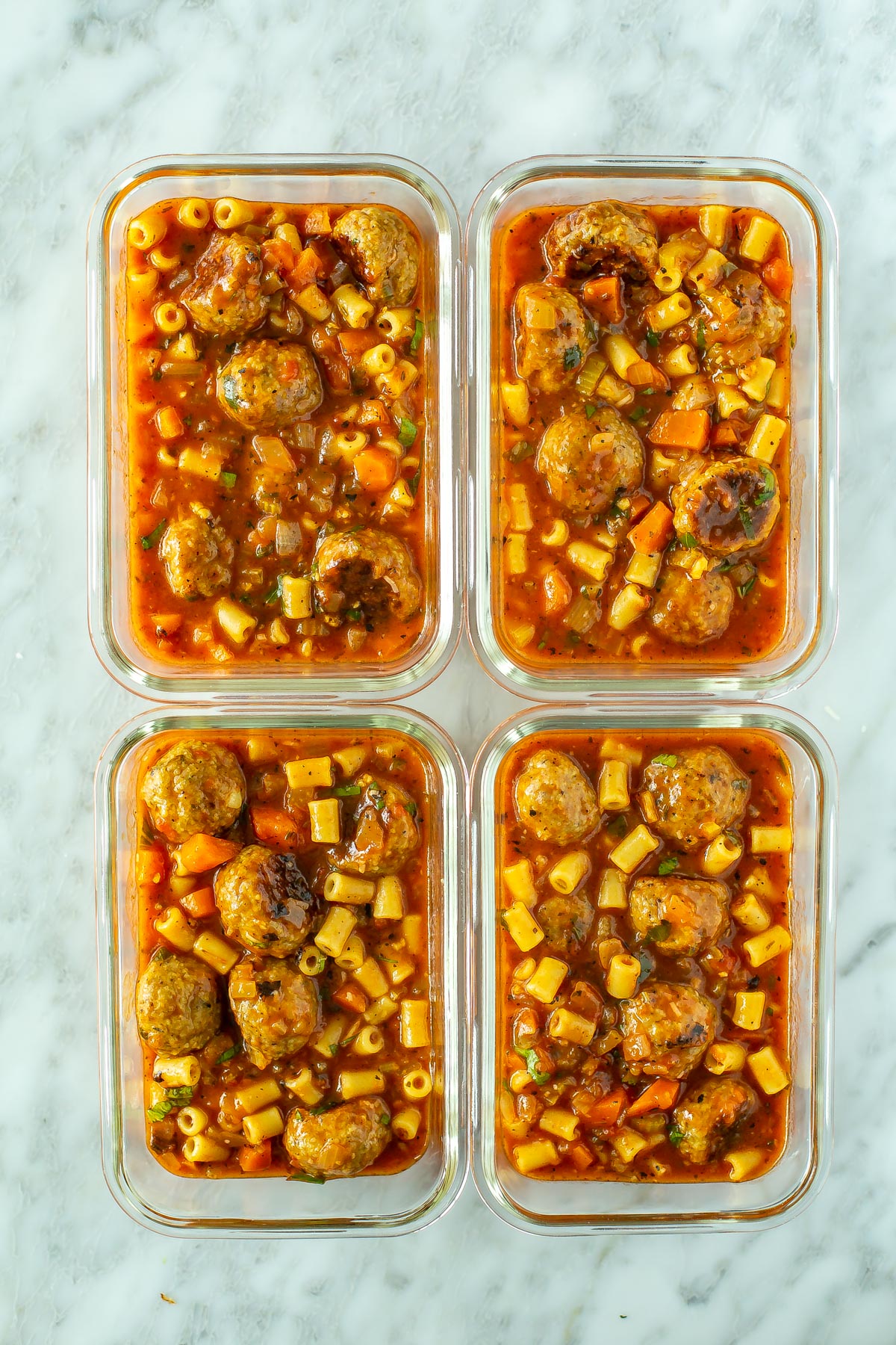 Four glass meal prep containers, each with a serving of Italian turkey meatball soup.