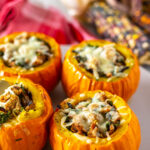 Four stuffed mini pumpkins in the foreground on a platter with fall decor in the background.