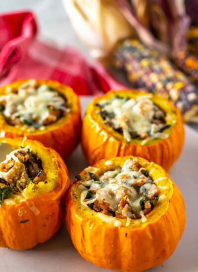 Four stuffed mini pumpkins in the foreground on a platter with fall decor in the background.