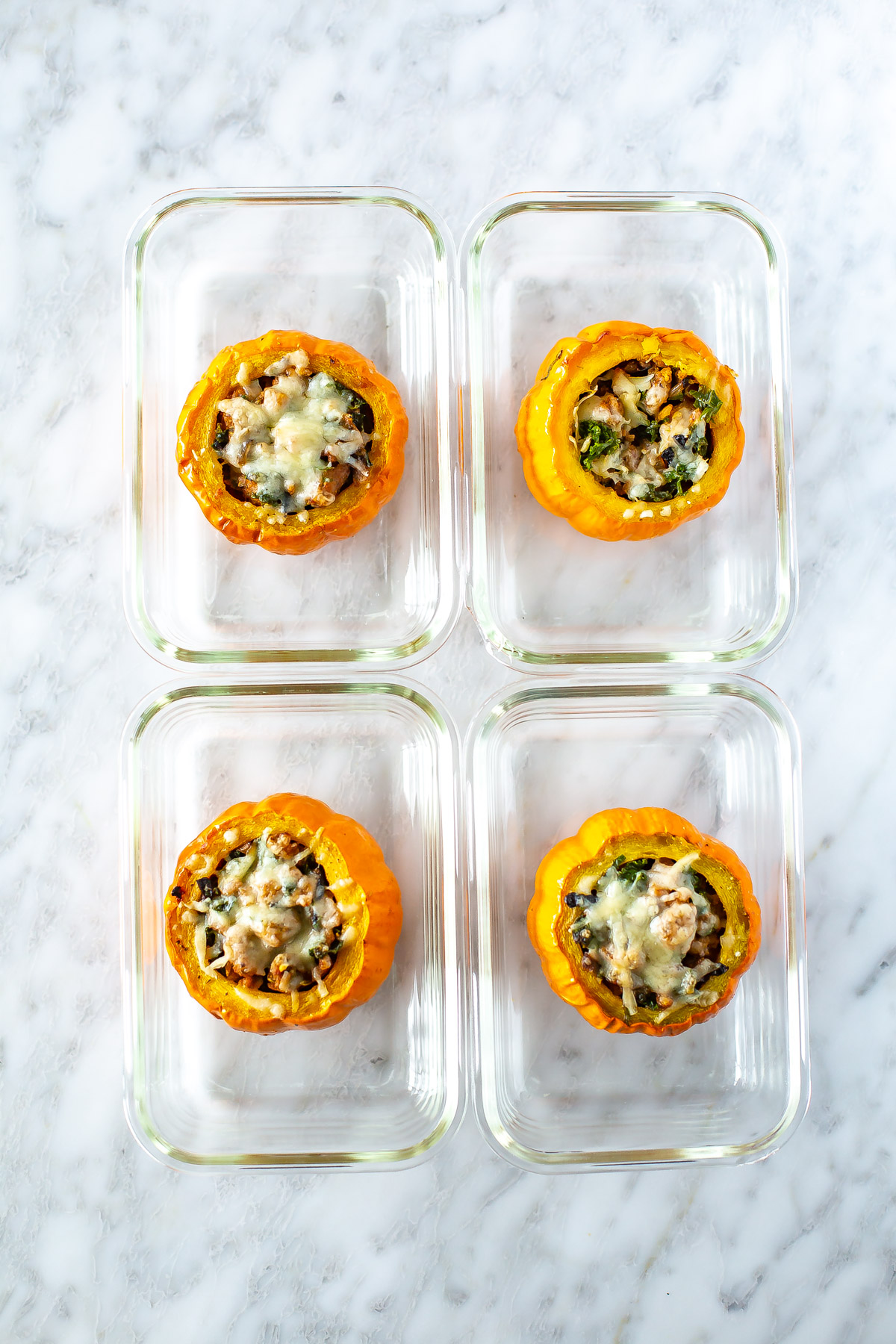 Four meal prep containers, each with a mini stuffed pumpkin inside.