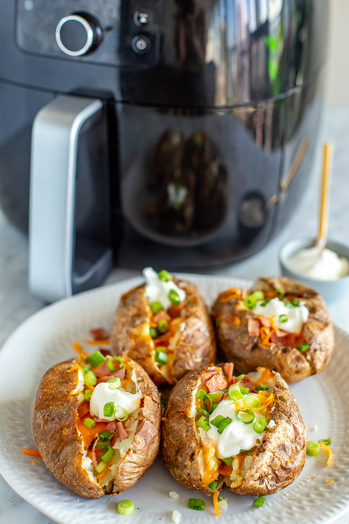 Four air fryer fully loaded baked potatoes in the foreground with an air fryer in the background.