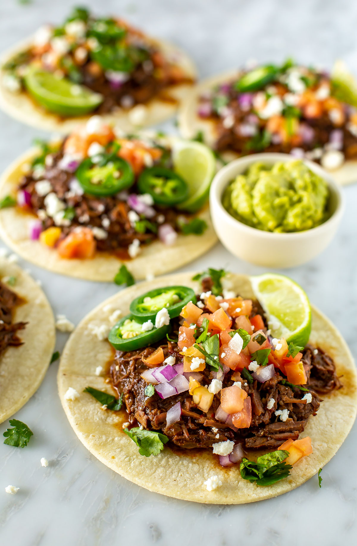 Four shredded beef tacos with a cup of guacamole on the side.