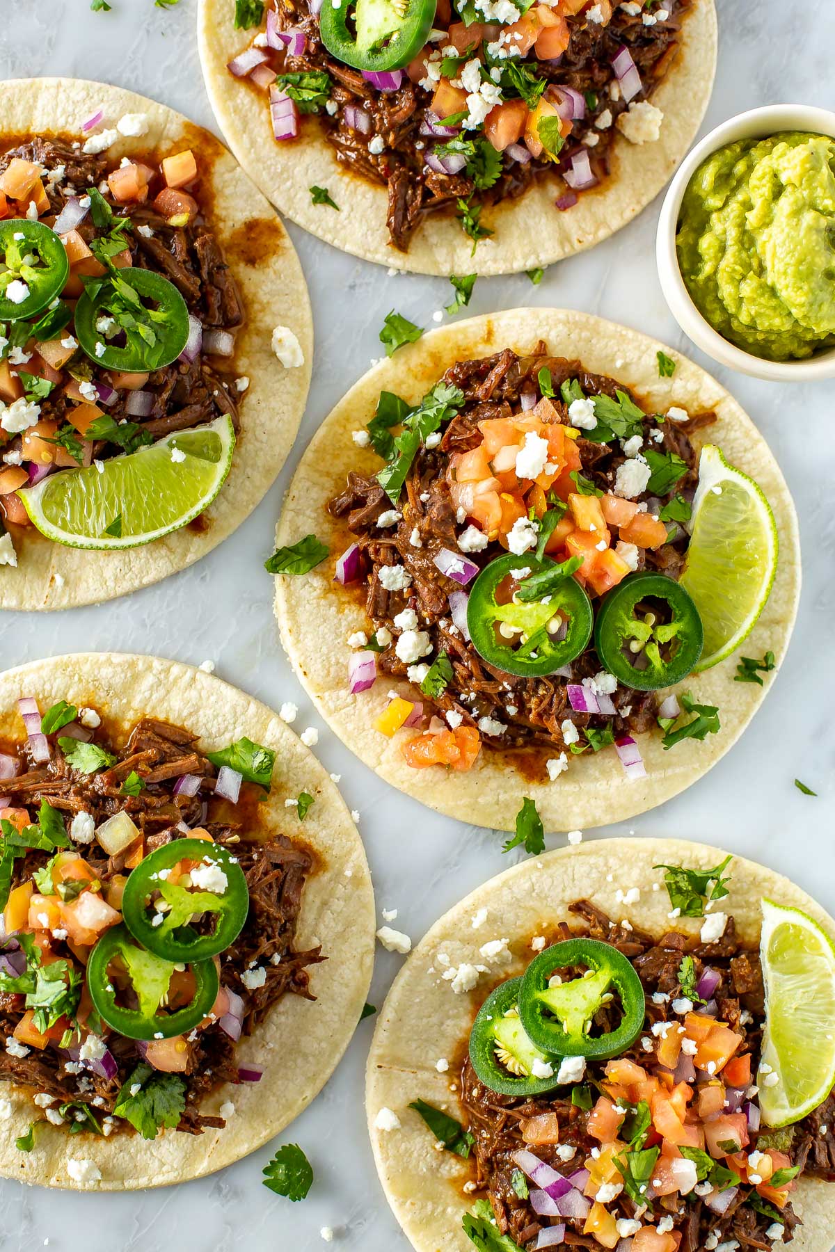 Five shredded beef tacos, each with an assortment of toppings on top.