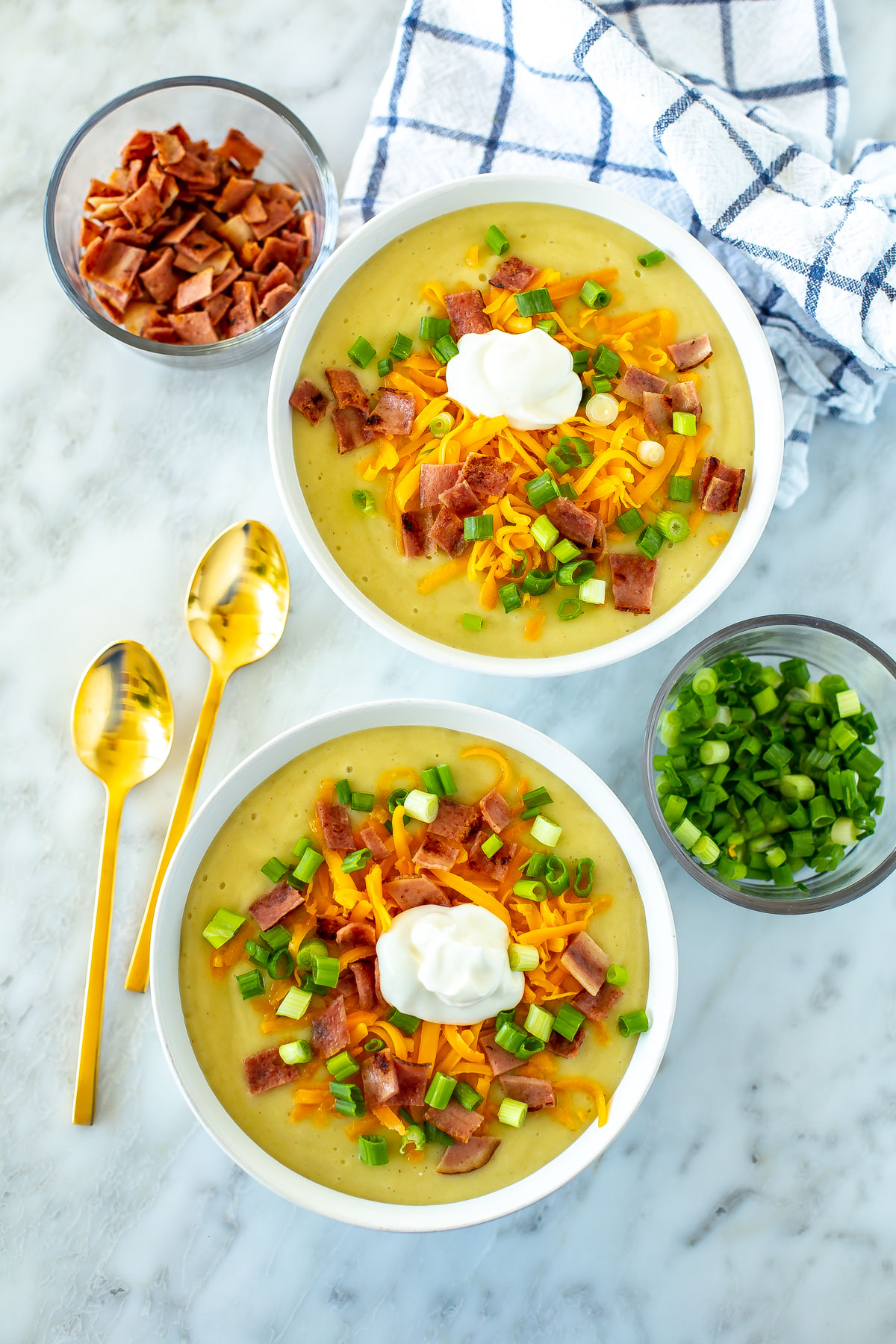 Two bowls of crockpot potato soup topped with cheddar cheese, bacon, green onions and sour cream.