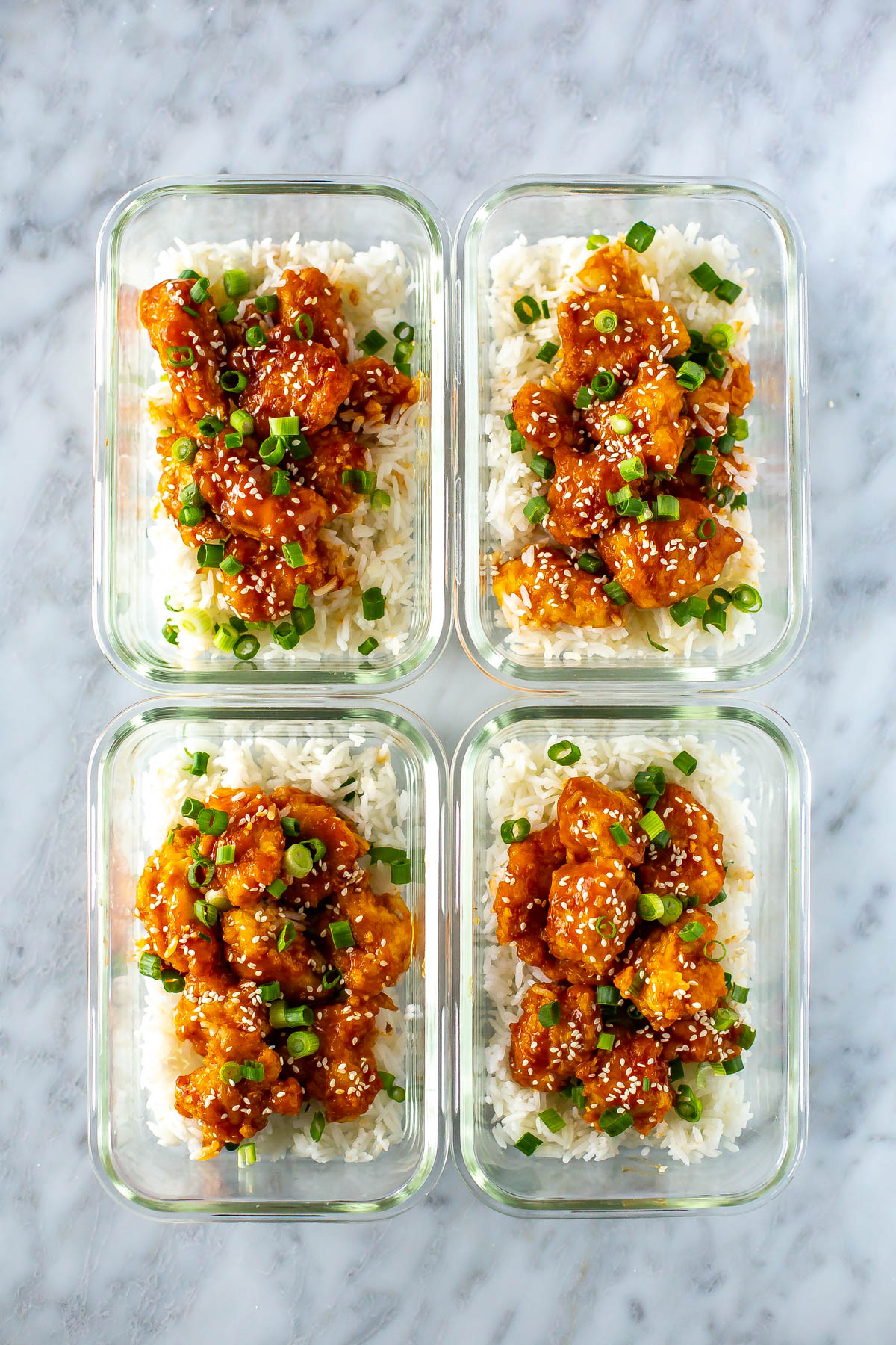 Four meal prep containers, each filled with rice and topped with crispy mandarin chicken.