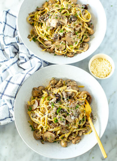 Two bowls of creamy mushroom pasta with a small bowl of parmesan cheese on the side.