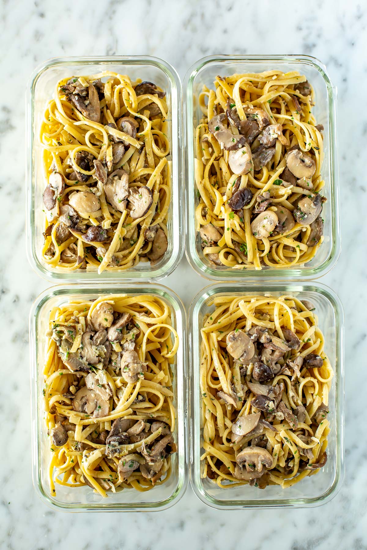 Four meal prep containers, each filled with creamy mushroom pasta.