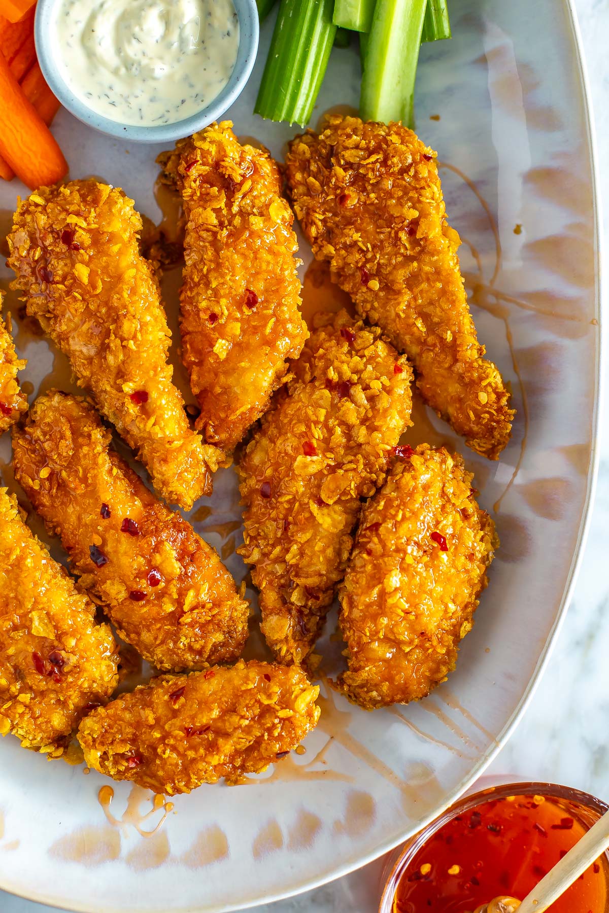 A close-up of air fryer hot honey chicken tenders on a platter with a bowl of hot honey off to the side.