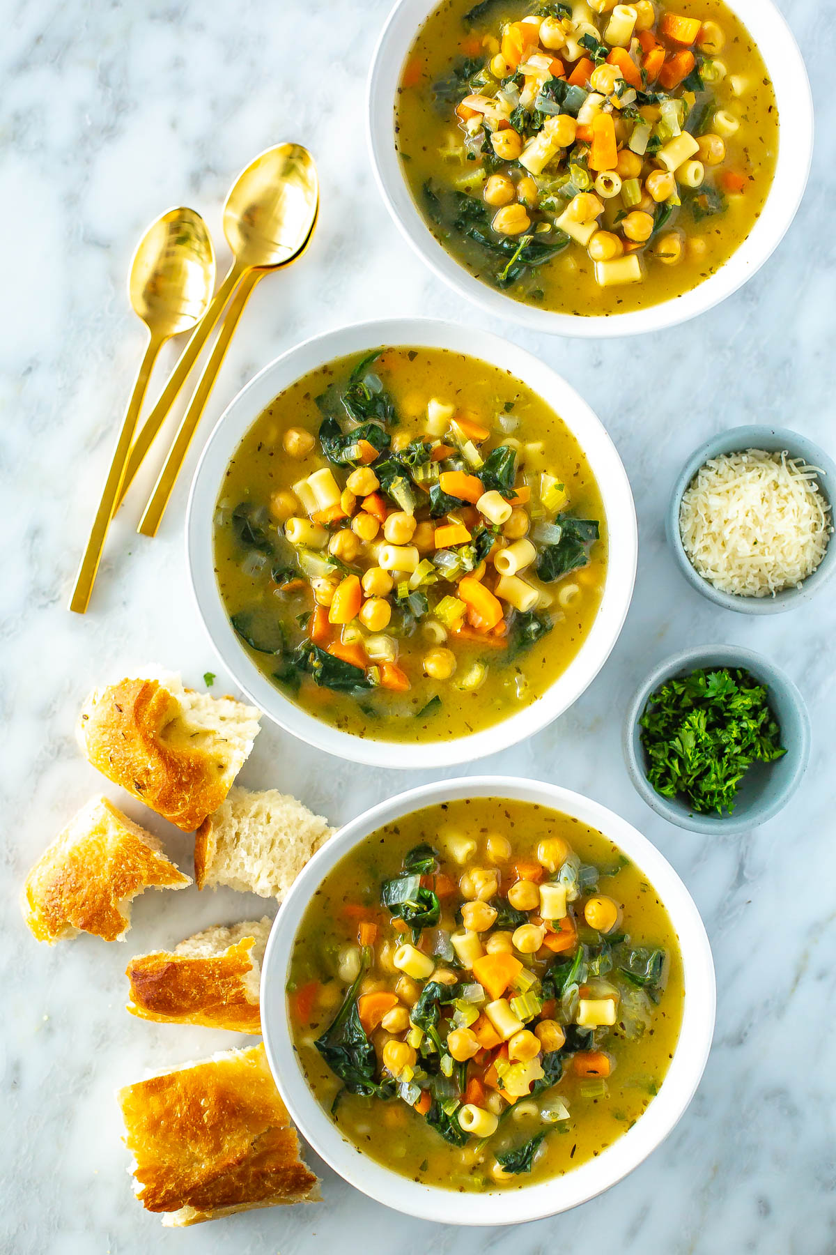 Three bowls filled with chickpea soup with some pieces of bread on the side.