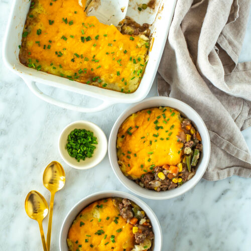 A casserole dish with classic shepherd's pie with two pieces of it in individual bowls.