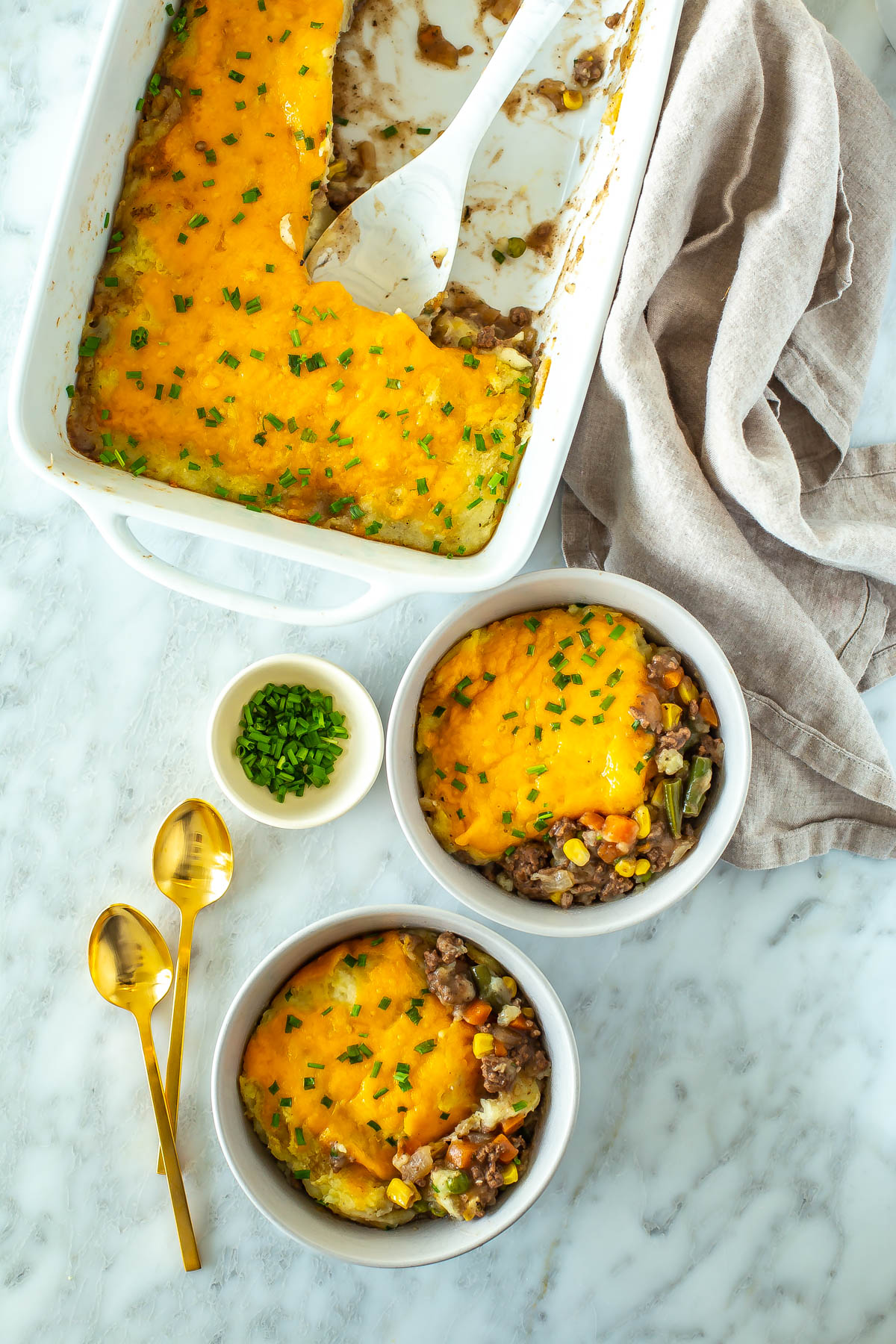 A casserole dish with classic shepherd's pie with two pieces of it in individual bowls.