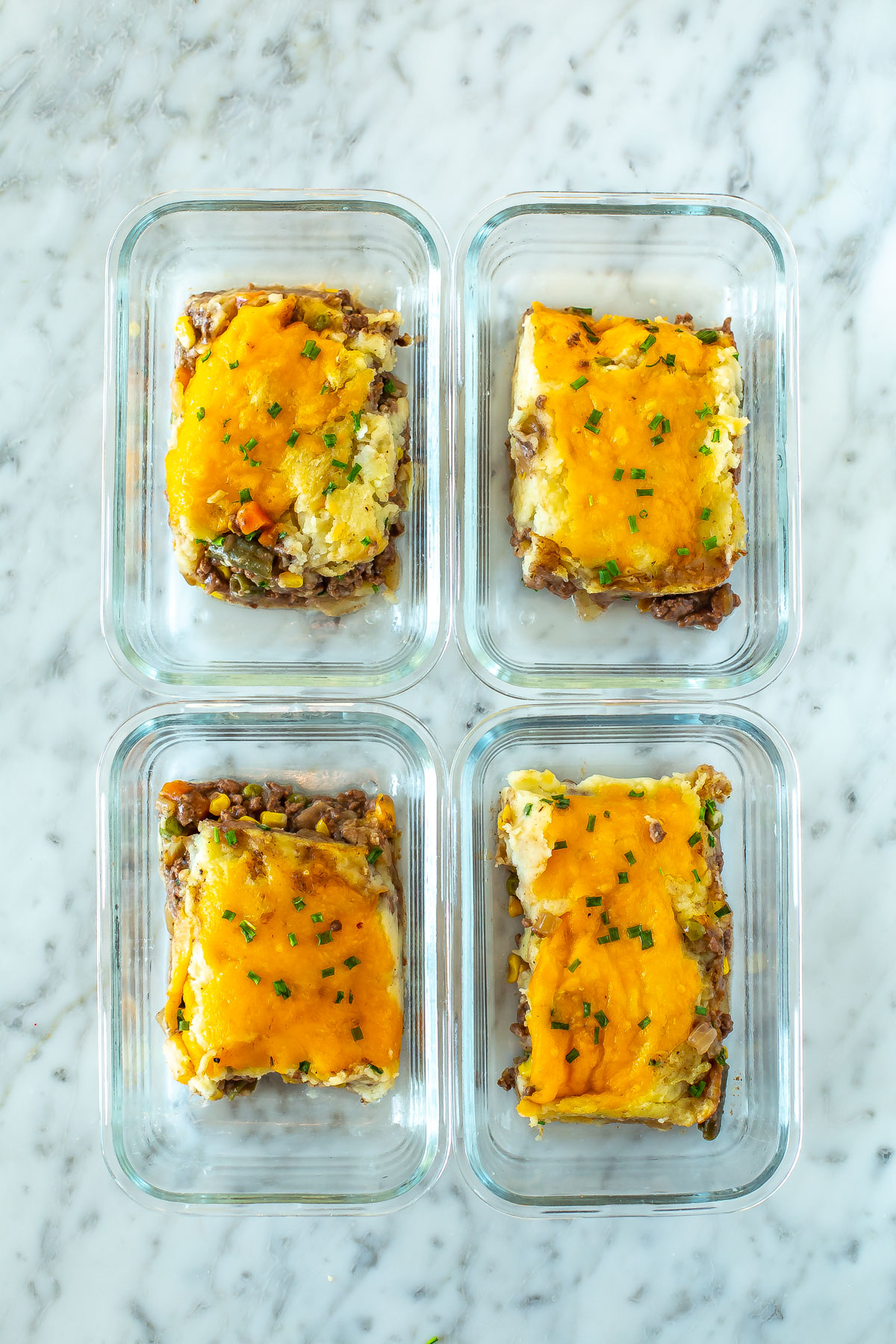 Four meal prep containers, each with a piece of classic shepherd's pie inside.