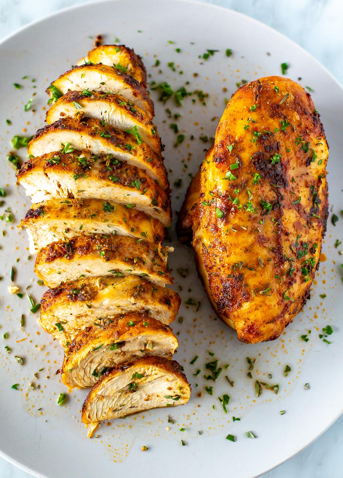 A close-up of a plate with one whole air fryer chicken breasts and another one that has been sliced.