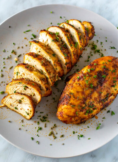 A plate with one whole air fryer chicken breast and another one that has been sliced.