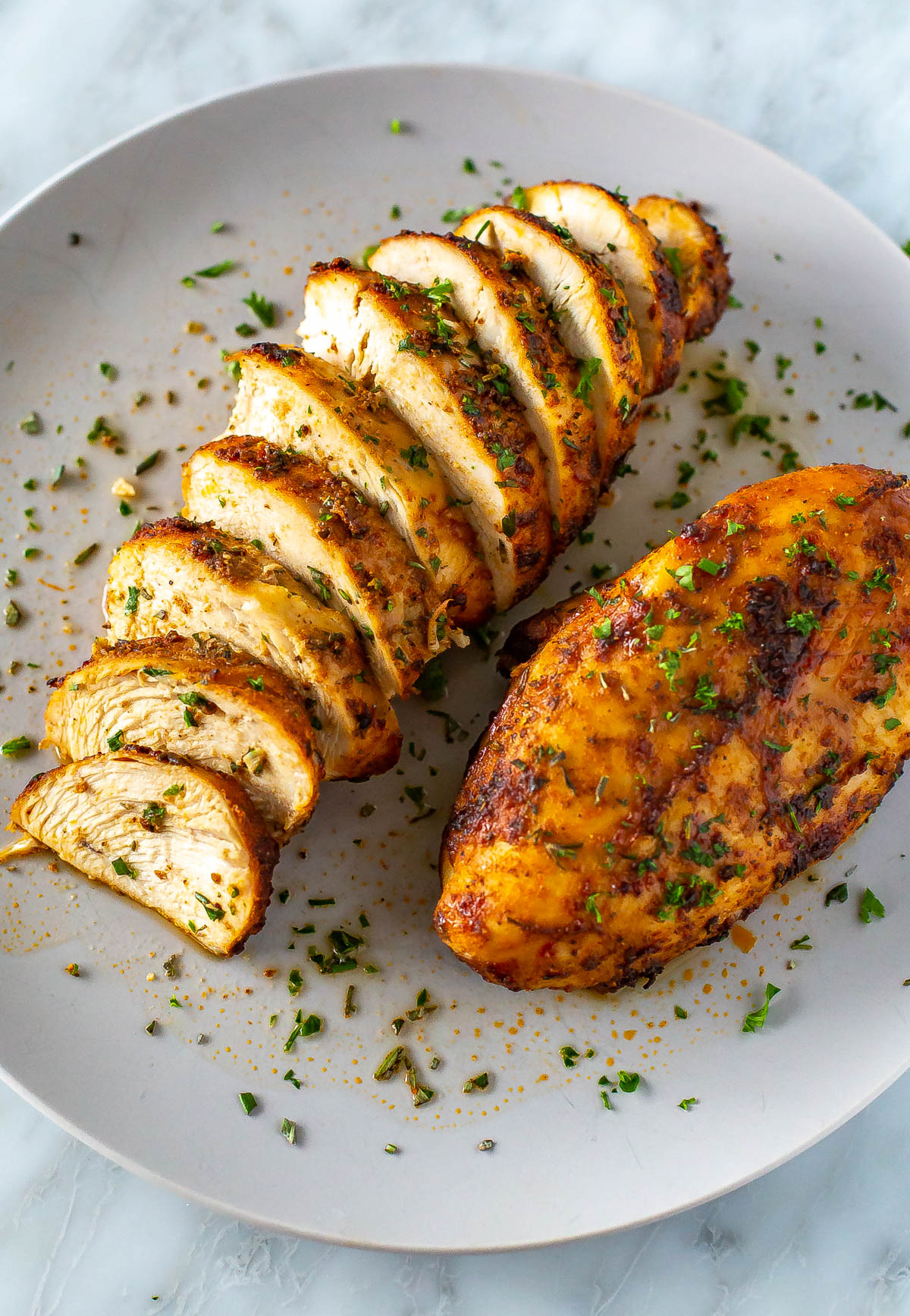 A plate with one whole air fryer chicken breast and another one that has been sliced.