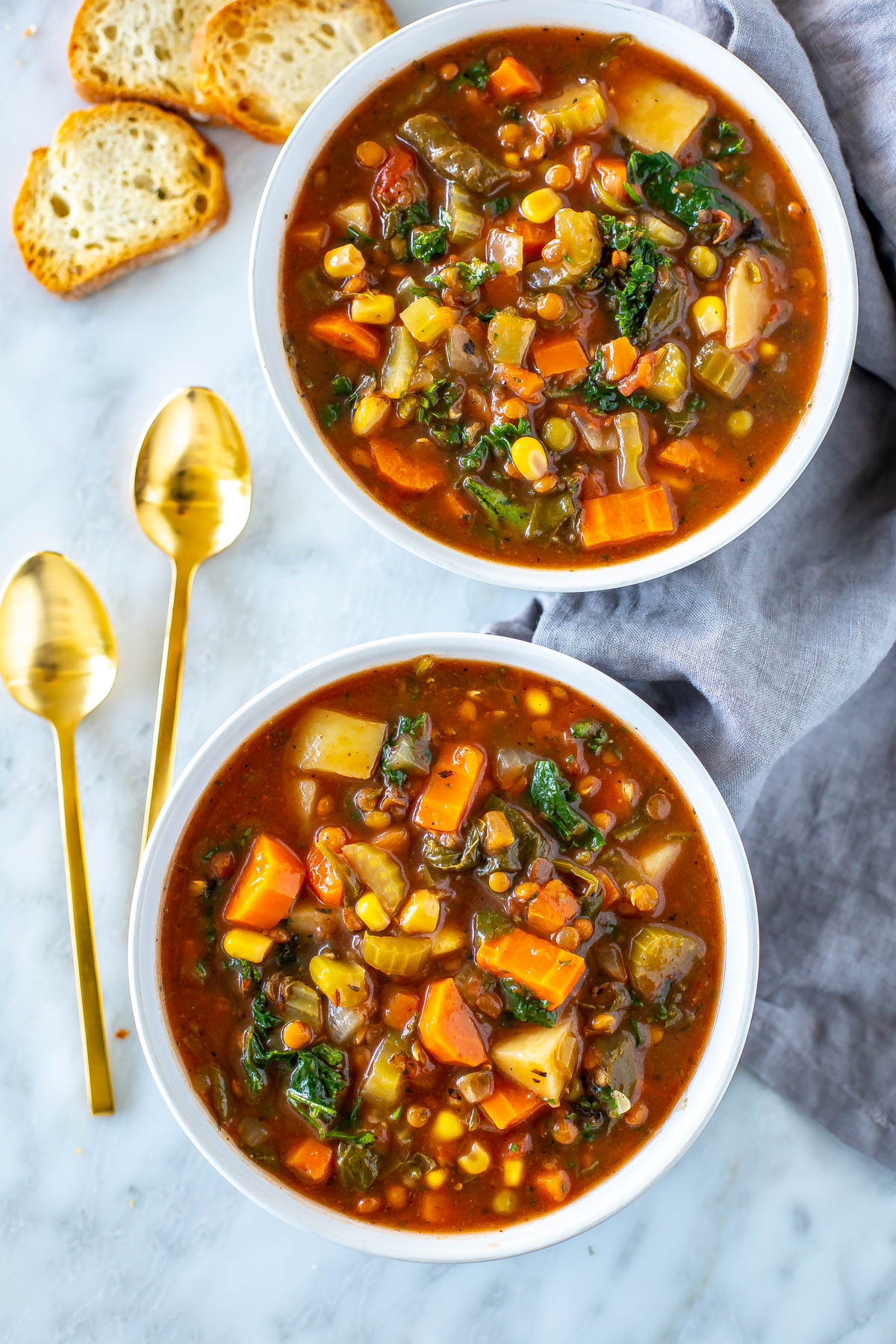 Two bowls of crockpot vegetable soup with spoons on the side.