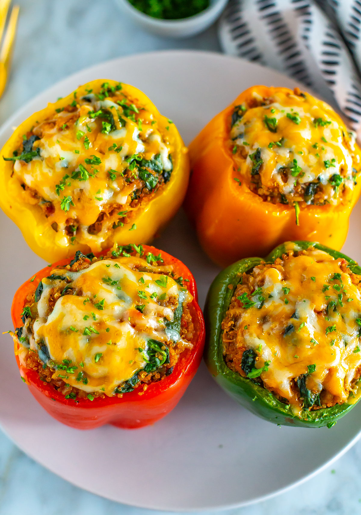 Four air fryer stuffed peppers on a plate, topped with cheese.