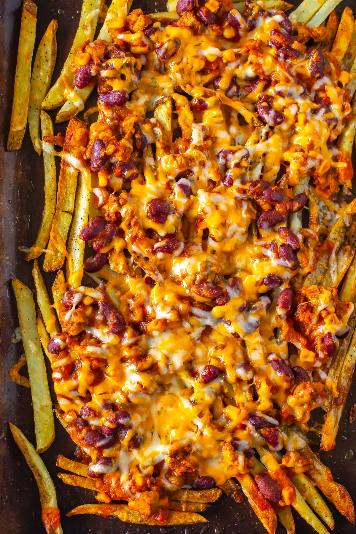 A close-up of chili cheese fries on a sheet pan lined with parchment paper.