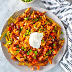 A big plate with chili cheese fries on top, loaded with tomato, green onions and sour cream.