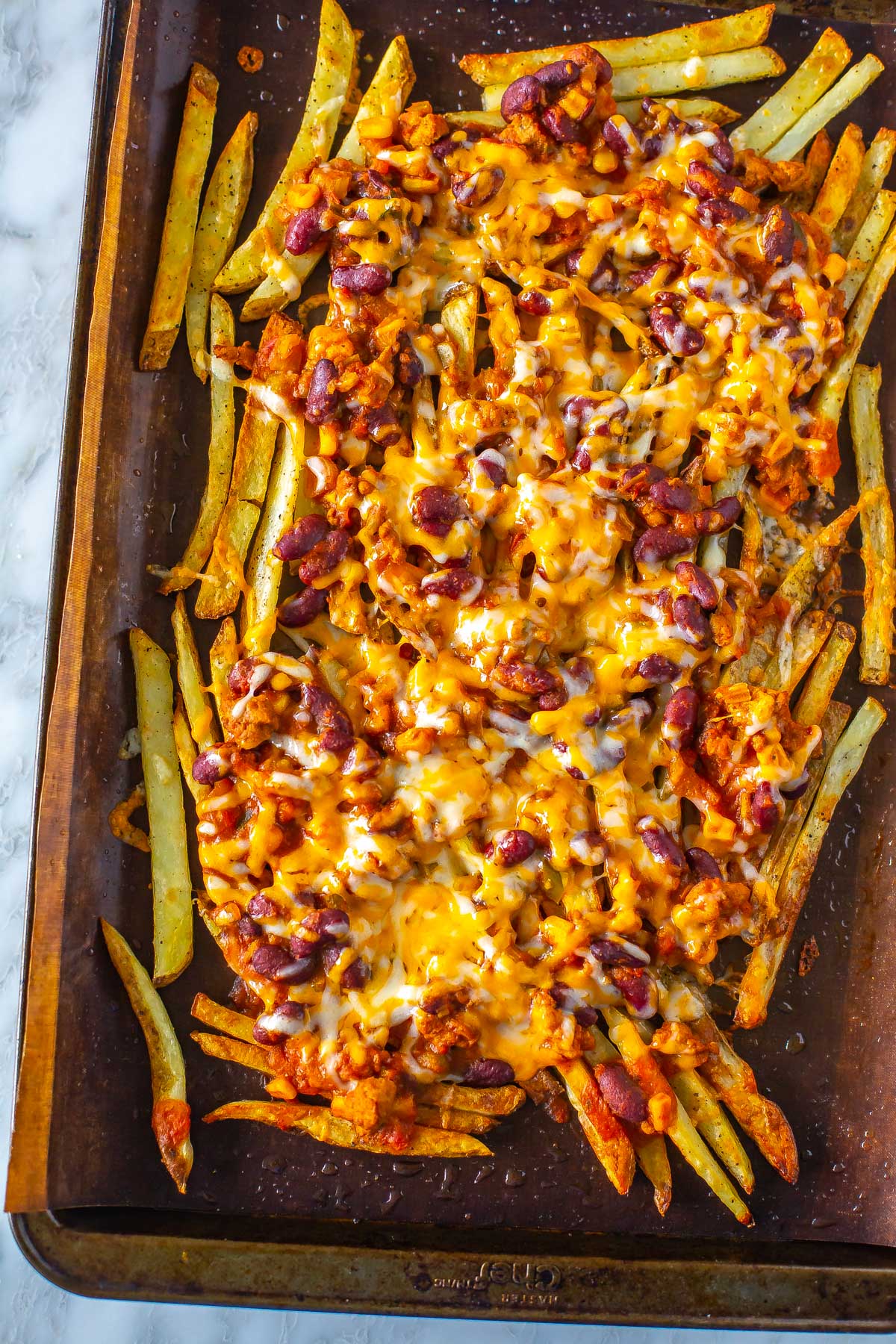 A close-up of chili cheese fries on a sheet pan lined with parchment paper.
