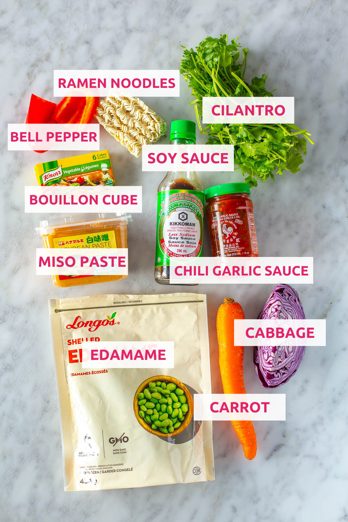 Ingredients for DIY instant noodles: ramen noodles, cilantro, bell pepper, chili garlic sauce, soy sauce, edamame, bouillon cube, carrot, and cabbage.