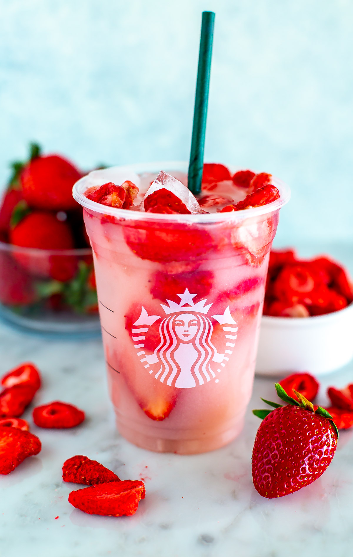 A glass of homemade Starbucks pink drink surrounded by strawberries.