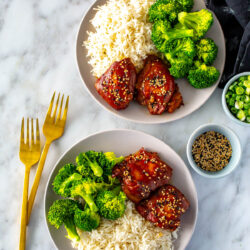 Two plates with slow cooker honey garlic chicken thighs served with broccoli and rice.