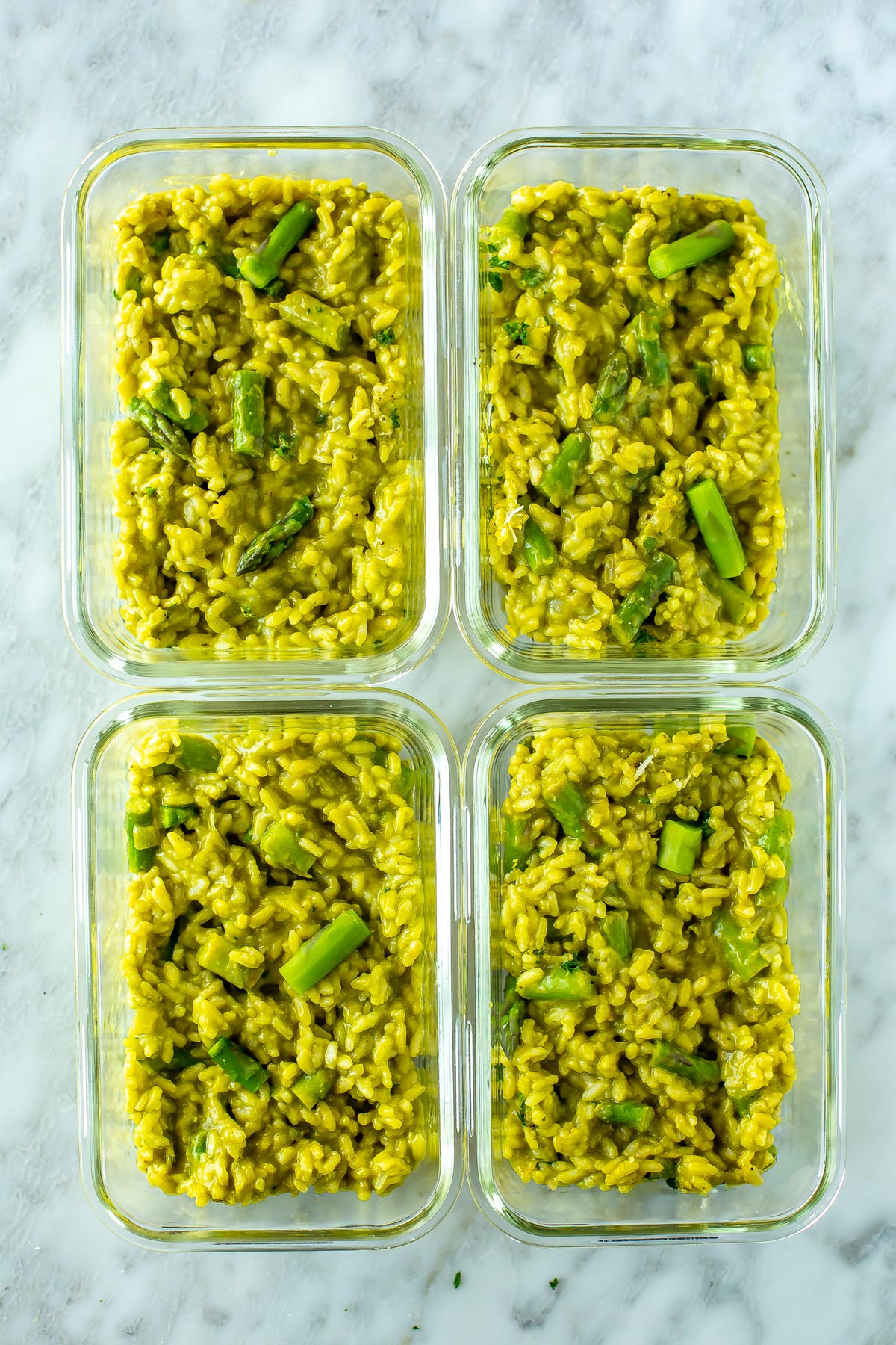 Four meal prep containers, each with a serving of asparagus risotto.
