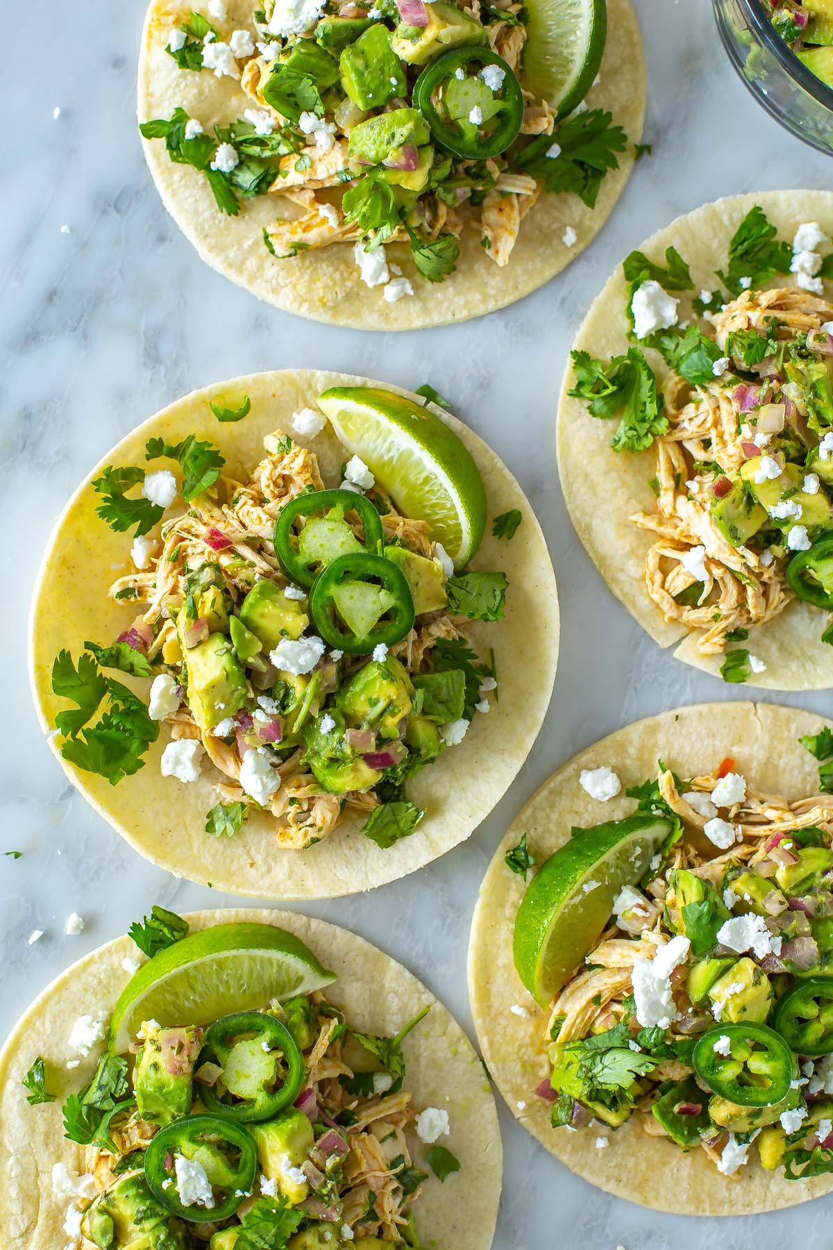 A close-up of cilantro lime chicken tacos with a bowl of avocado salsa placed next to them.