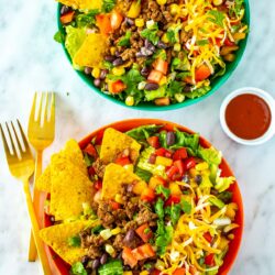 Two bowls of dorito taco salad with extra taco sauce on the side.