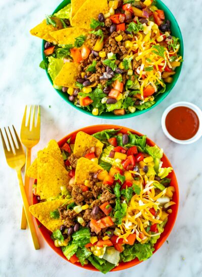 Two bowls of dorito taco salad with extra taco sauce on the side.