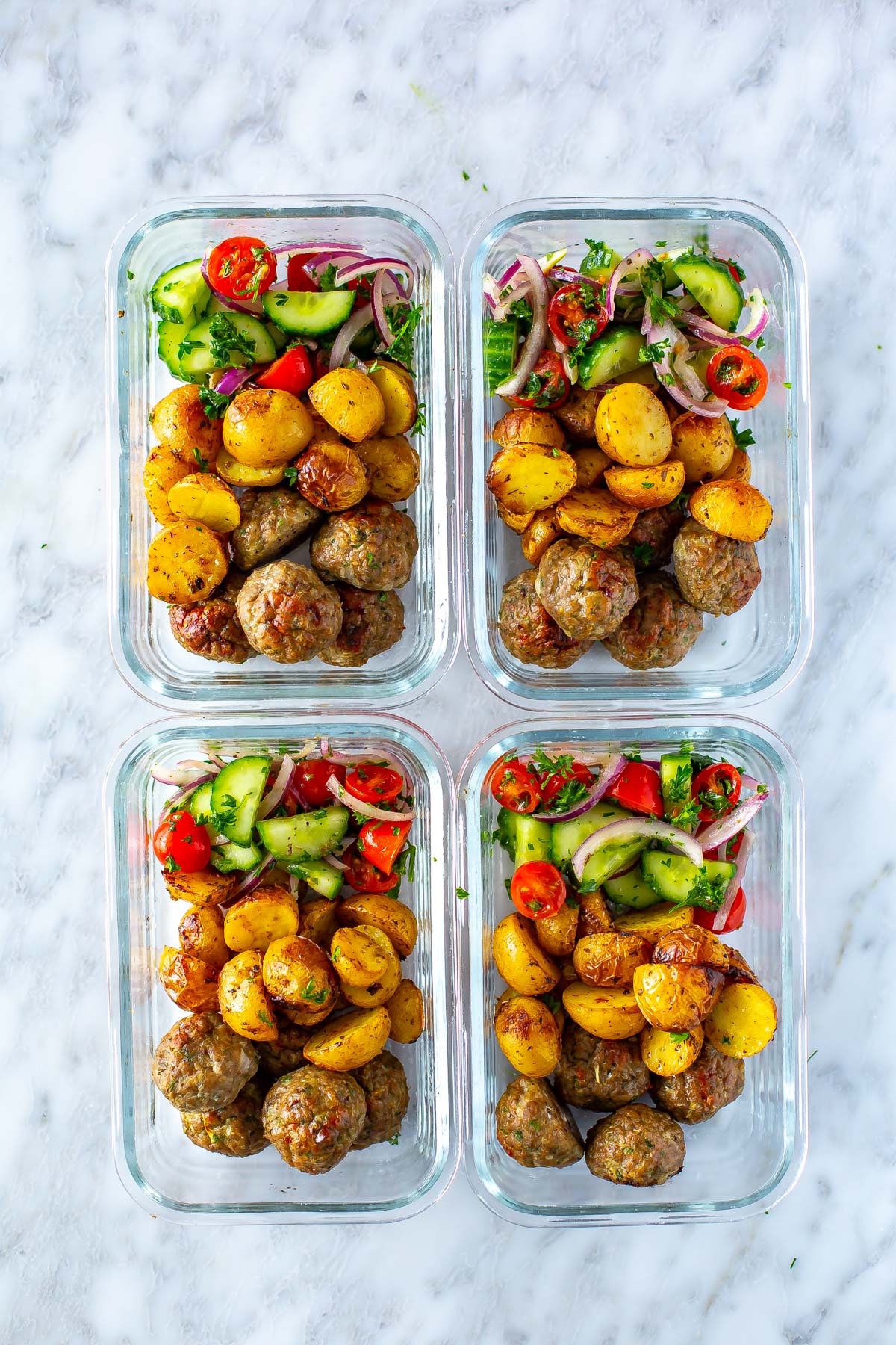 Four meal prep containers, each with a serving of greek meatballs, potatoes and a side of veggies.